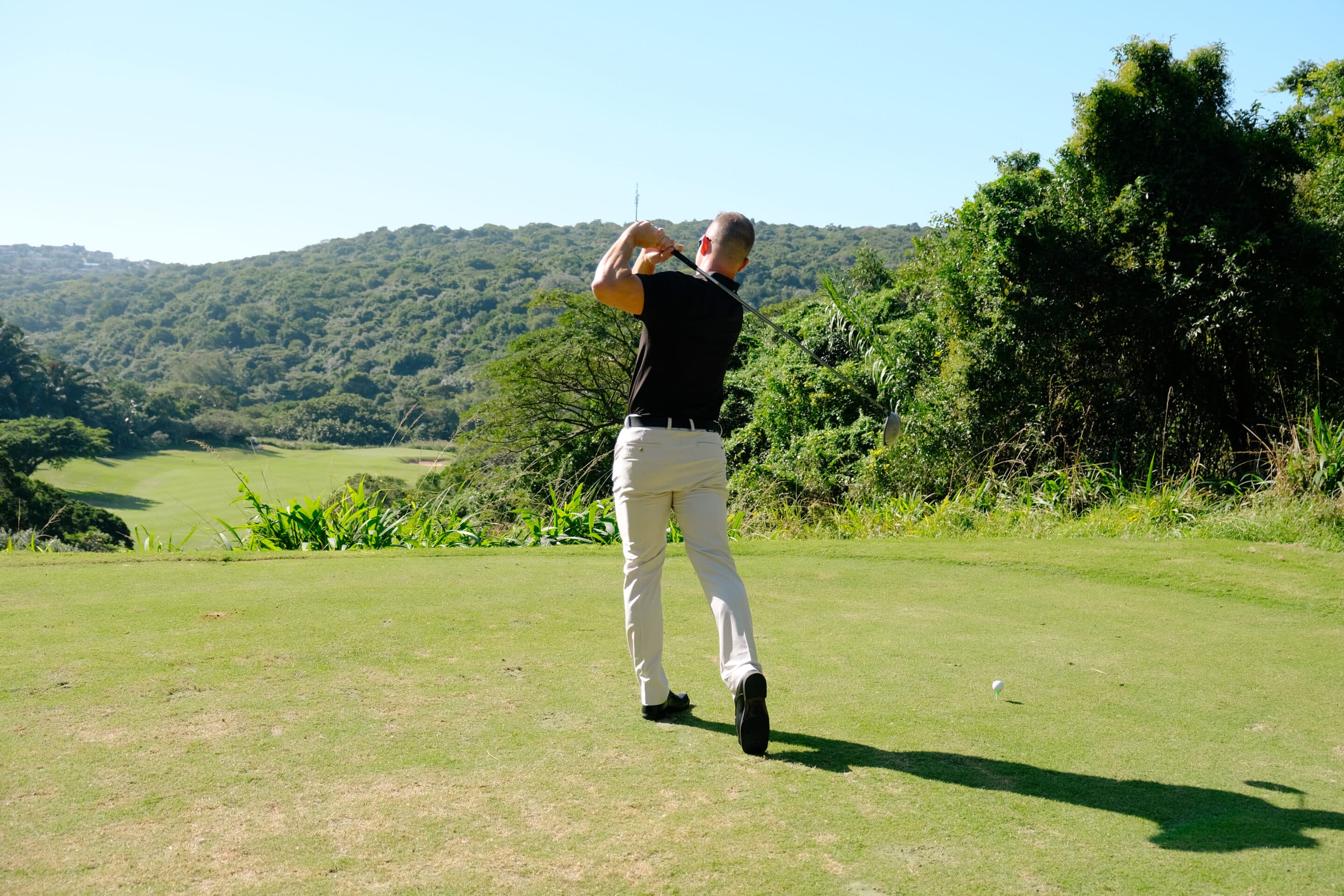 Golfer taking a tee shot on a lush green golf course surrounded by trees and hills